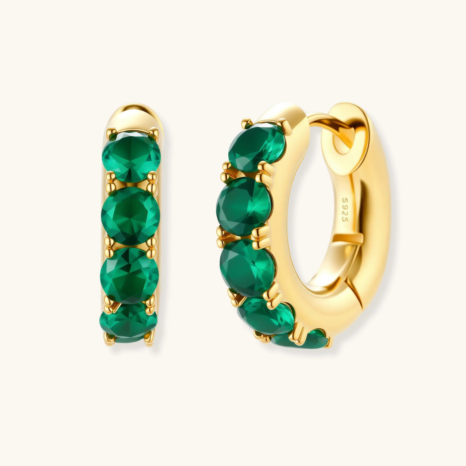 Close-up of gold-plated huggie hoop earrings featuring four emerald green cubic zirconia stones on white background.