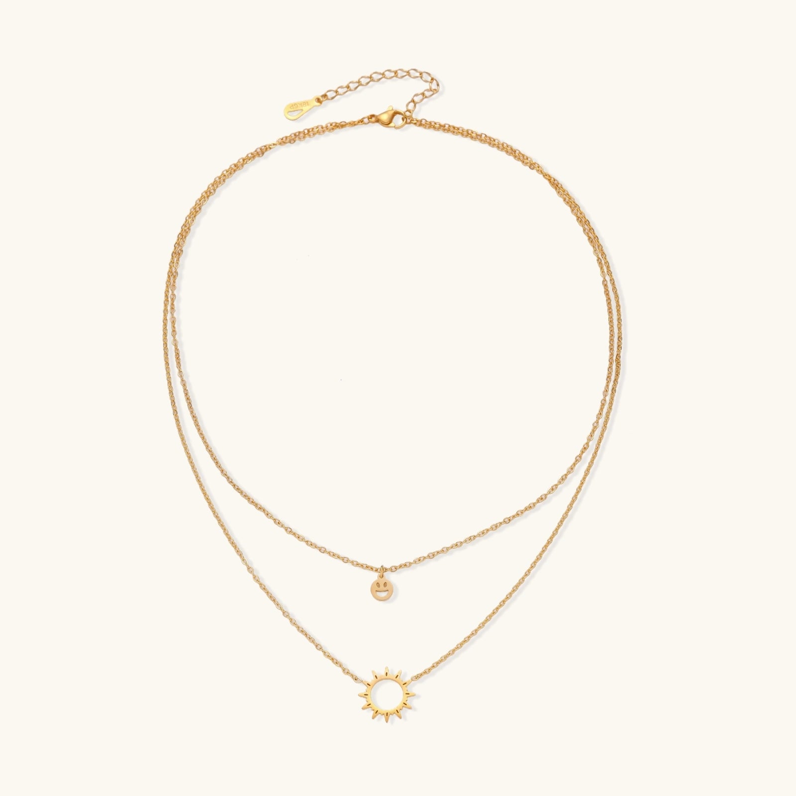 Gold layered necklace set with sunburst and smiley face pendants on delicate chains against white background.